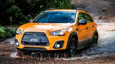 the front end of a yellow car driving through muddy road with trees in the background