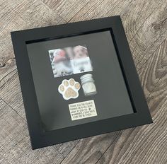 a black frame with some pictures and dog paw magnets on the inside, sitting on a wooden floor