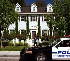 a police car parked in front of a white house with a woman standing on the roof