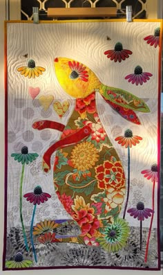 a quilted rabbit with flowers and butterflies on it's back, hanging from a wall