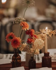 three vases with flowers are sitting on a table in front of candles and napkins