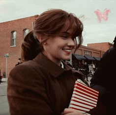 a woman holding an american flag in her hands and smiling at the camera with a butterfly flying overhead