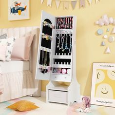 a white jewelry cabinet sitting on top of a bed next to a wall with pictures