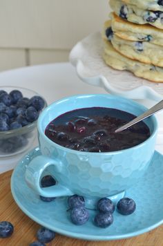 a bowl of blueberry soup on a plate with some pancakes in the back ground