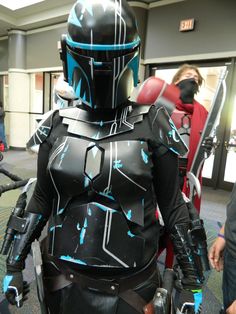 a man dressed up in a star wars costume standing next to another person wearing a helmet and holding two swords