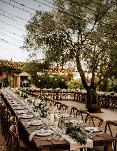 a long table set up with place settings and greenery for an outdoor wedding reception