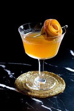 an orange drink in a glass on a black table with a gold coaster around it