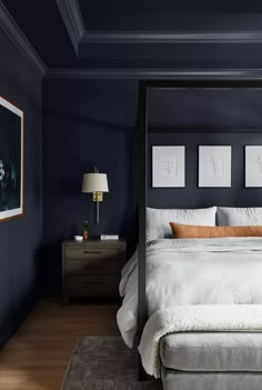 a bedroom with dark blue walls and white bedding, two nightstands, an art print on the wall