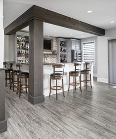 an open concept kitchen and living room with wood flooring, bar stools and built - in cabinets