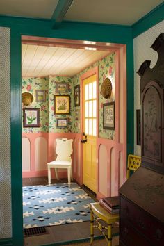 the interior of a house with pink walls and green trimmings, including a white chair