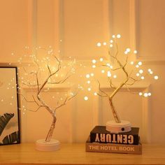 two small trees with white lights on top of a wooden table next to a framed photograph