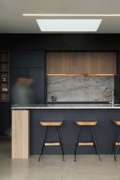 three stools sit in front of an island with marble countertops and black cabinets