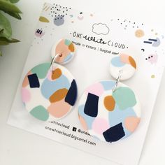 a pair of multicolored earrings sitting on top of a white table next to a potted plant