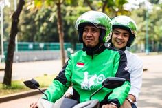 two people riding on the back of a motor scooter in green and white