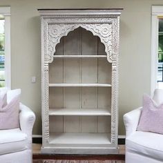 a living room with two white chairs and a bookcase in the middle of it