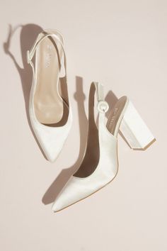 two pairs of white high heeled shoes on top of a pink surface, with one shoe in the middle