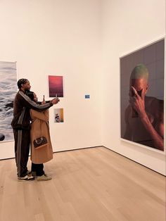 two people standing in an art gallery looking at pictures on the wall and touching their hands