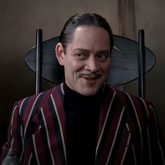 a man sitting in a chair with a mustache on his face and wearing a striped suit