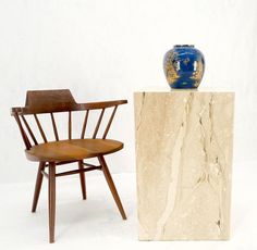 a wooden chair next to a blue vase on top of a marble block