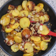 cooked potatoes and onions in a skillet with a red spoon sitting on the side