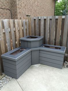 three planters are placed on the concrete in front of a brick wall and wooden fence