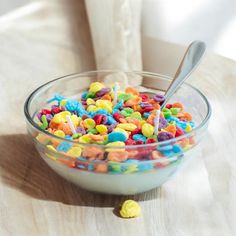 a glass bowl filled with cereal on top of a wooden table next to a spoon