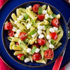 a pasta salad with tomatoes, mozzarella and spinach on a blue plate