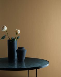 two black vases with white flowers sitting on a round table in front of a yellow wall