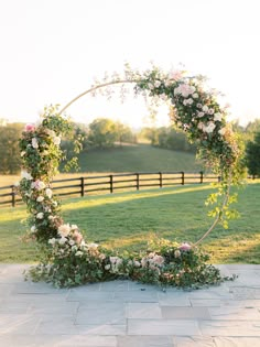 a wedding arch with flowers and greenery on the ground in front of a fence