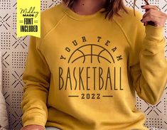 a woman wearing a yellow sweatshirt with the words your team basketball on it