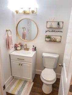 a white toilet sitting next to a sink in a bathroom under a round mirror with gold accents