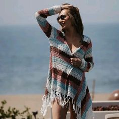 a woman standing on the beach with her hand in her hair and wearing a multicolored crocheted poncho