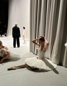 two ballerinas are sitting on the floor in front of curtained drapes