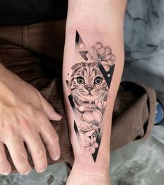 a cat tattoo on the arm with flowers and triangles around it's face,