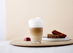 a cup of coffee and some food on a tray next to a plate with two pieces of cake