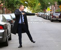 a man in a suit and tie is pointing at something on the street near parked cars