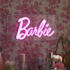 a pink neon sign that says barbie on it's glass shelf next to other items