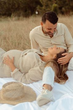 a man and woman laying on top of a white blanket in the middle of a field