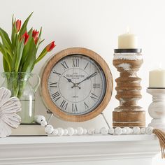 a clock sitting on top of a mantle next to candles and flowers in vases