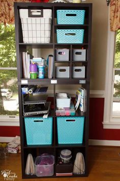 a book shelf with baskets and other items on it in front of a windowsill