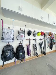 there are many backpacks and ski poles hanging on the wall in this garage area