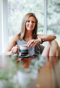 a woman sitting at a table holding a coffee cup