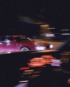 a red car driving down a street at night