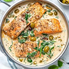 two cooked salmon fillets in a creamy white sauce with olives and capers