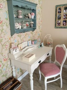 a white desk with pink chairs in front of a wallpapered wall and a birdcage