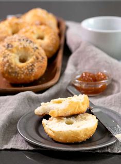 two bagels on a black plate with jam and spoons next to the table