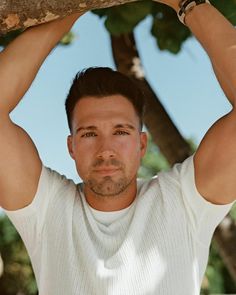 a man holding onto a tree branch with his hands over his head and looking at the camera