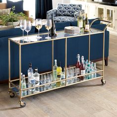 a bar cart with wine glasses and liquor bottles on it in front of a couch