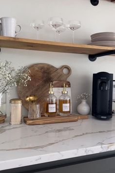 a kitchen counter topped with lots of bottles and glasses next to a wooden cutting board