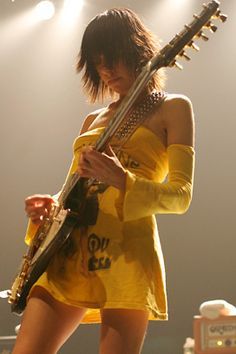 a woman in a yellow dress playing an electric guitar